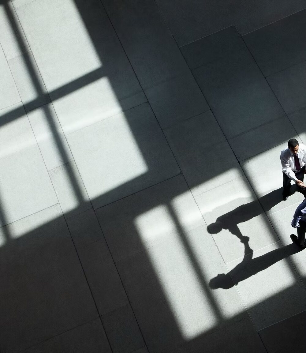 A lone figure crossing a sunlit plaza floor, seen from above